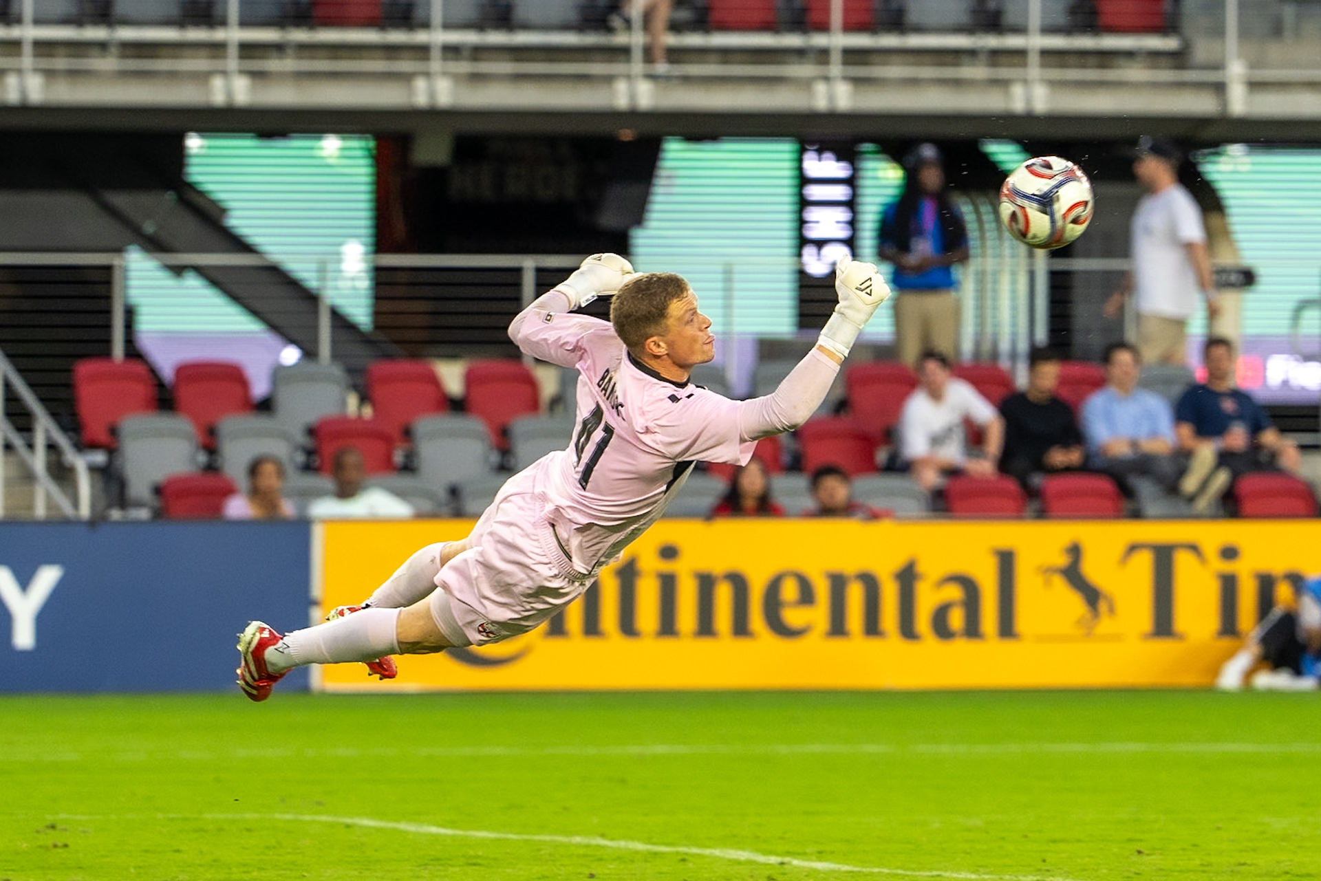 A goalkeeper in pink dives toward a soccer ball